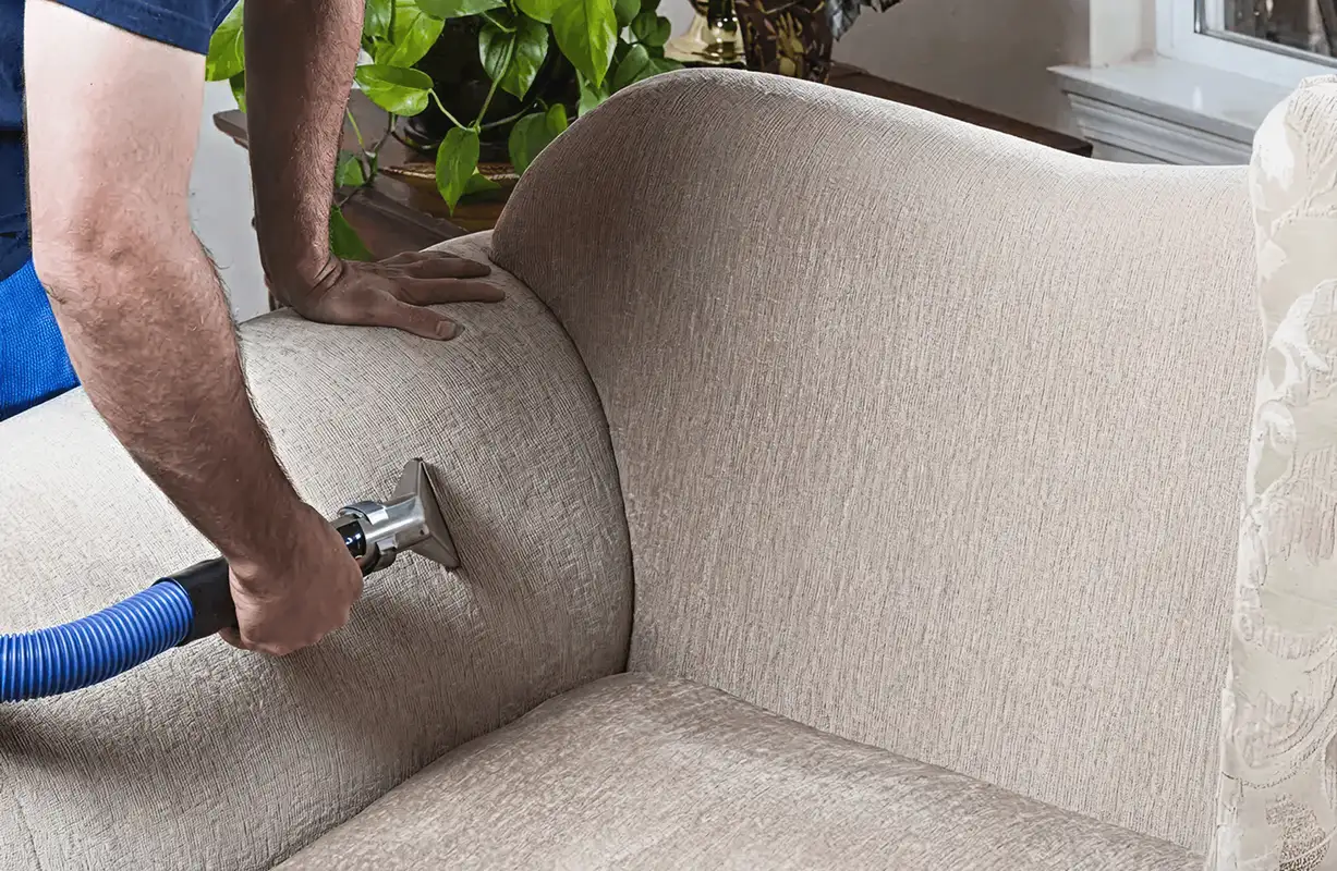 Professional upholstery cleaner deep-cleaning a fabric sofa with a handheld extraction tool and hose, Baltimore, MD.
